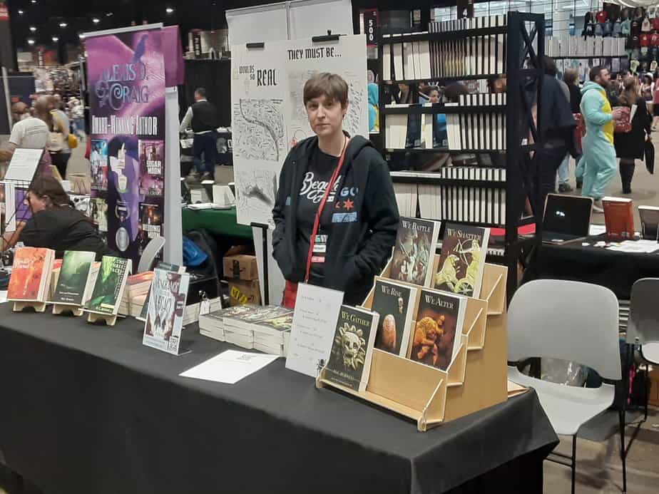 the author standing behind a table covered in piles of their own books